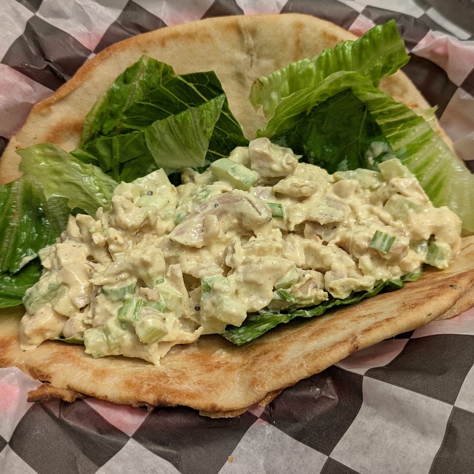 Flatbread topped with creamy chicken salad, chopped celery, and crisp romaine lettuce on checkered serving paper.