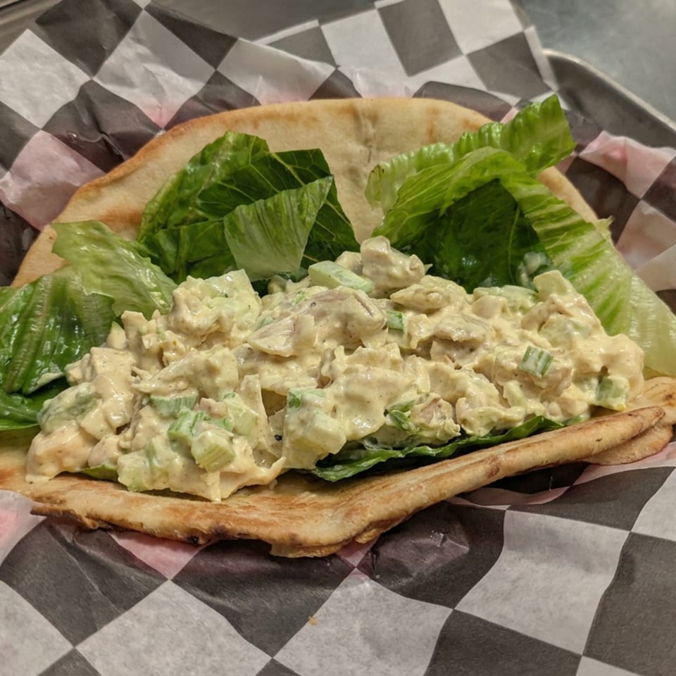 Creamy chicken salad with lettuce served on toasted flatbread in a checkered paper-lined metal tray.