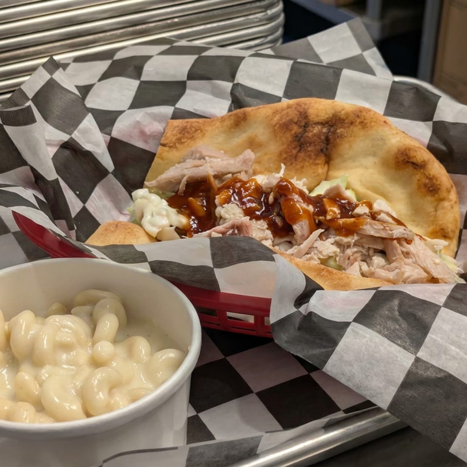 Pulled pork sandwich with barbecue sauce and creamy macaroni and cheese served on a checkered paper-lined tray.
