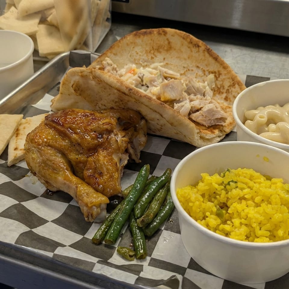 Tray featuring roasted chicken, flatbread, chicken salad pita, green beans, yellow rice, and macaroni and cheese.