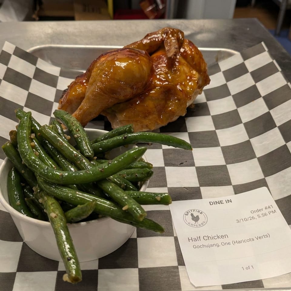 Glazed gochujang half chicken with seasoned green beans on a black-and-white checkered tray beside an order slip.